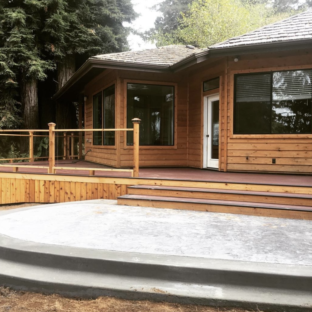 Beautiful home with a newly constructed wooden deck featuring glass railings and a concrete patio, a remodeling project by Mills Builds Inc. in Humboldt County, California.