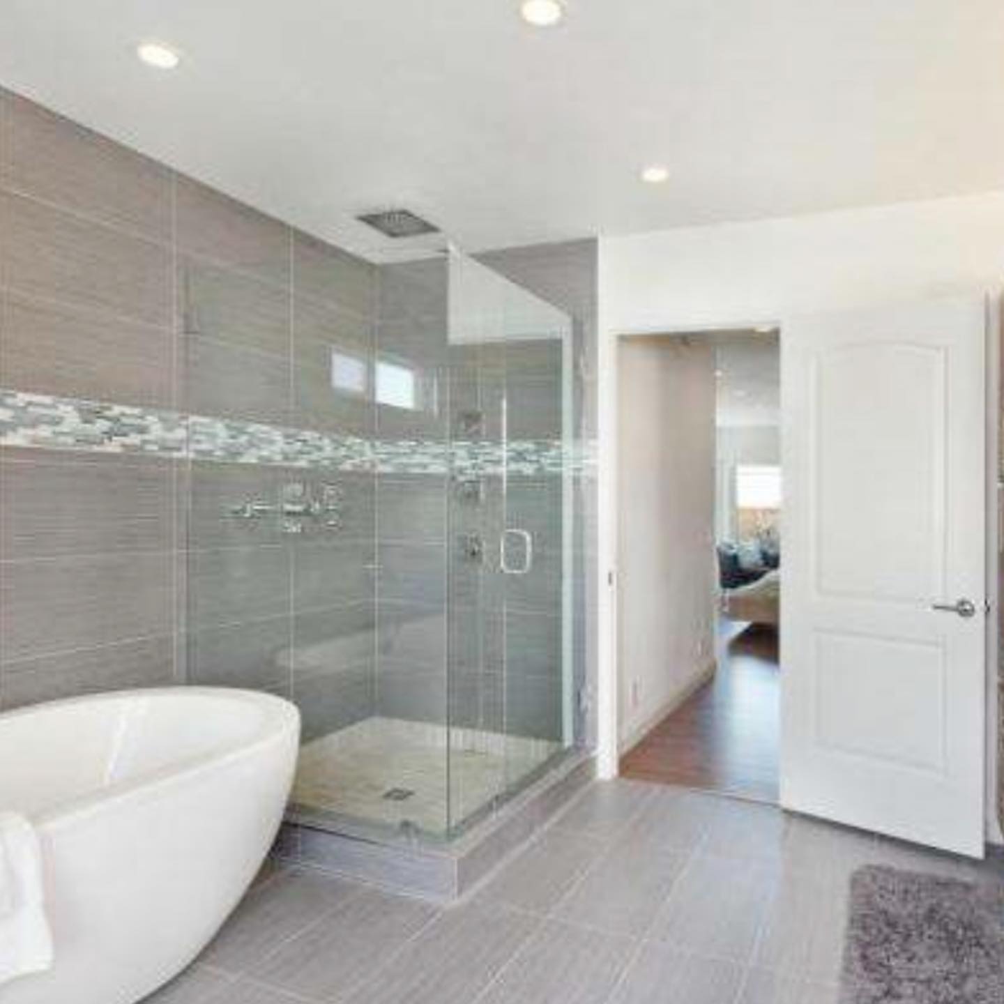 Modern custom bathroom designed by Mills Builds, featuring large grey tiles, glass shower enclosure, and freestanding soaking tub in a Humboldt County home.