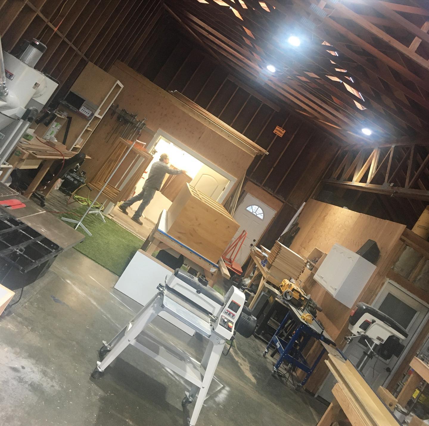 Interior view of the Mills Builds Inc. custom cabinet workshop with tools, lumber, and cabinets under construction.