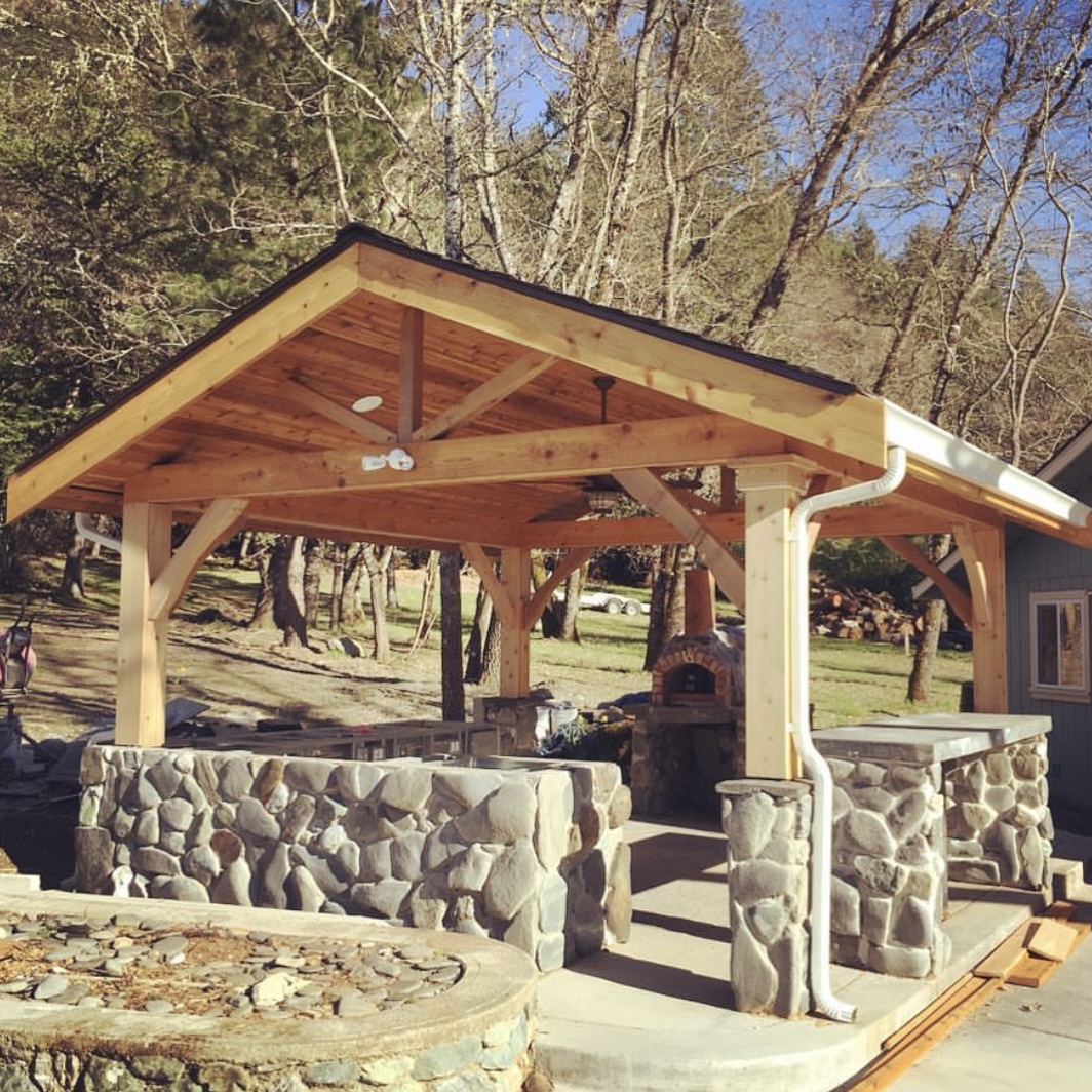 Custom-built outdoor kitchen and dining area with a wooden pergola and stone accents, a stunning project by Mills Builds Inc. in Humboldt County, California.