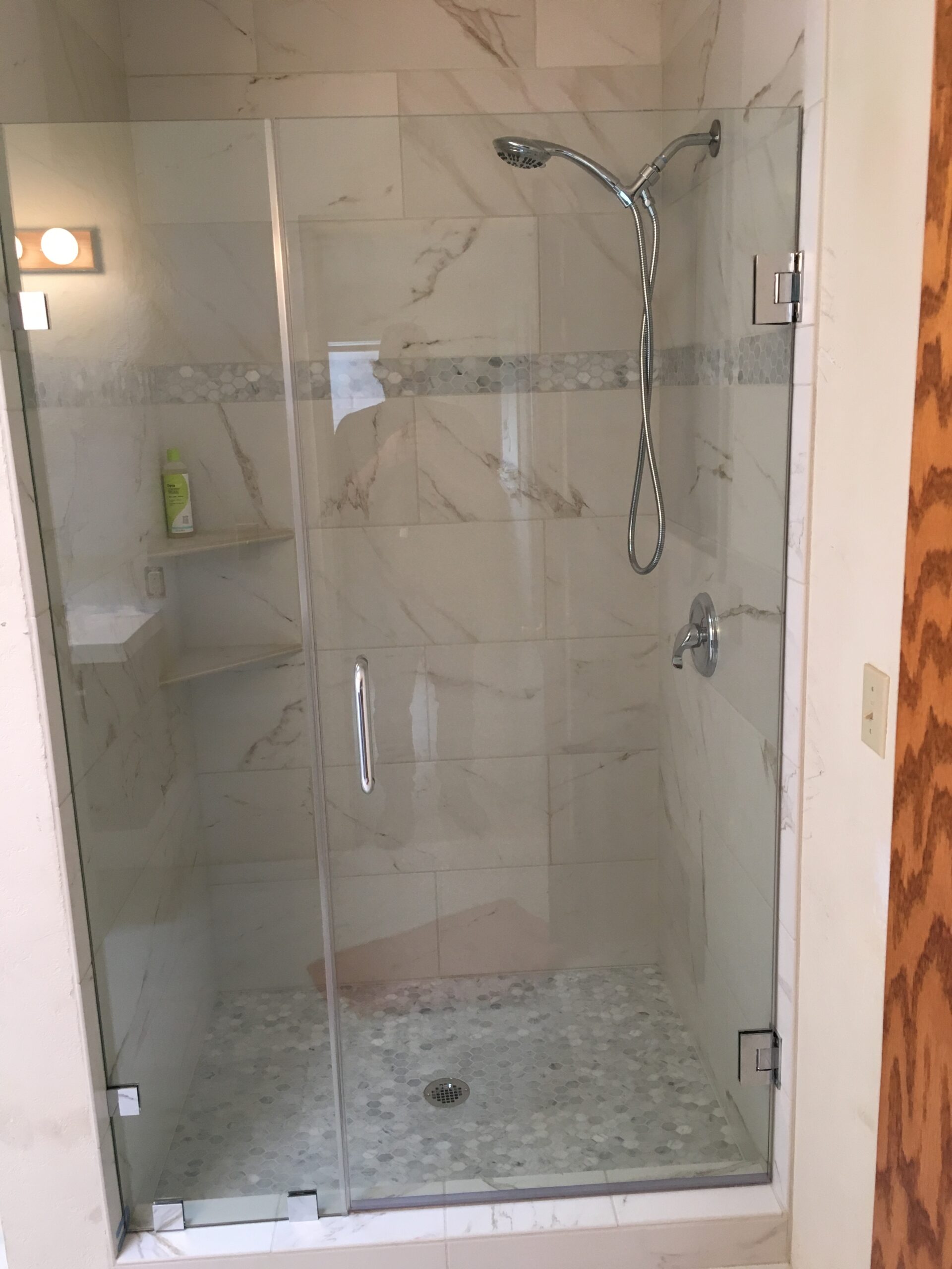 Frameless glass shower enclosure with swinging door and tile walls