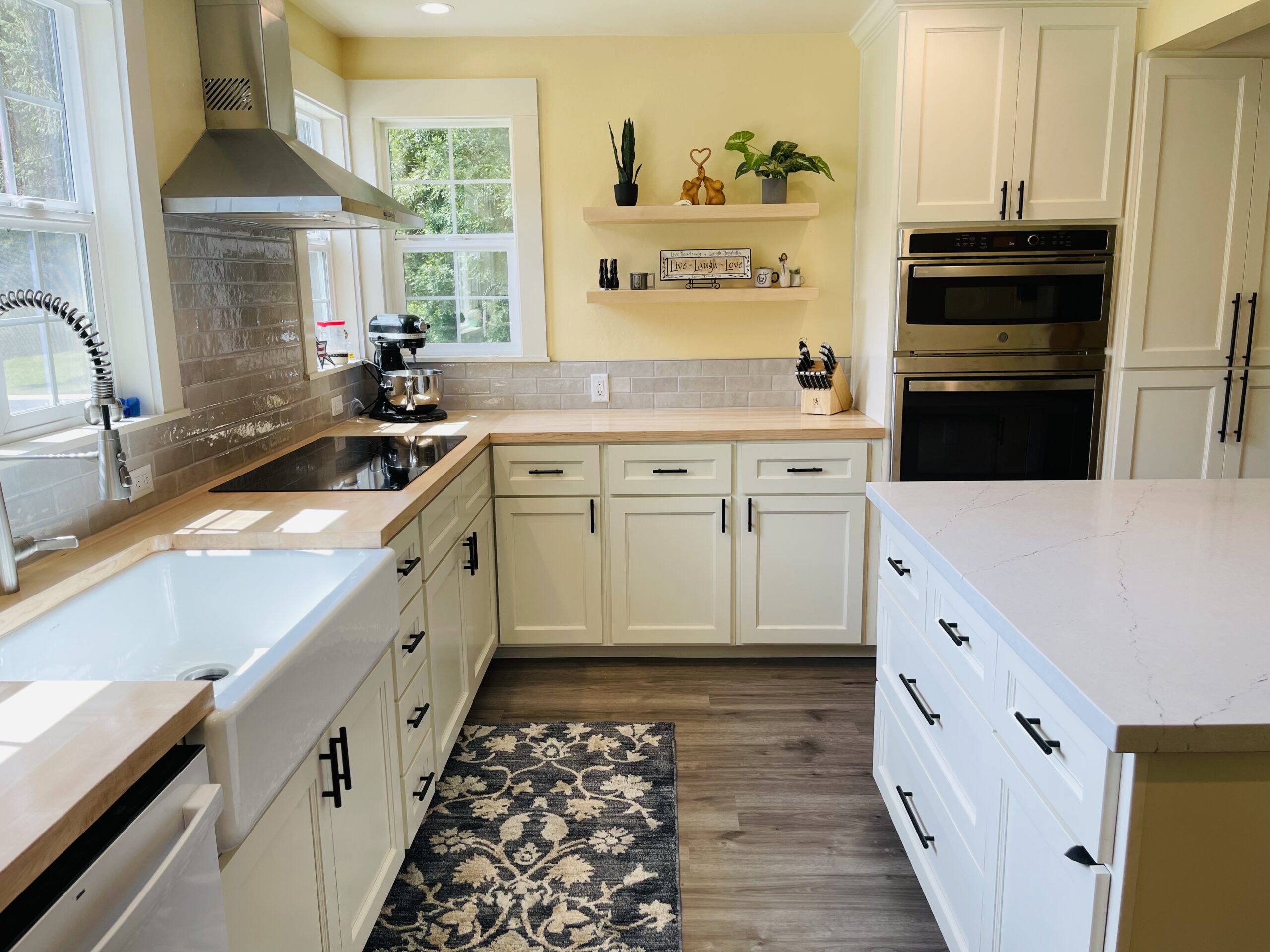 Bright modern kitchen with white shaker cabinets, light wood countertops, grey subway tile backsplash, and stainless steel range hood.